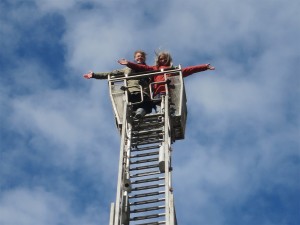Zwei Frauen am Ende einer hohen Leiter vor blauem Himmel