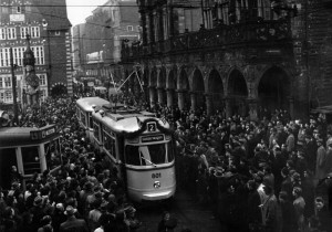 Historisches Bild mit Sambawagen und einer Menschenmenge, die vor dem Rathaus für eine neue Bahn Spalier steht.