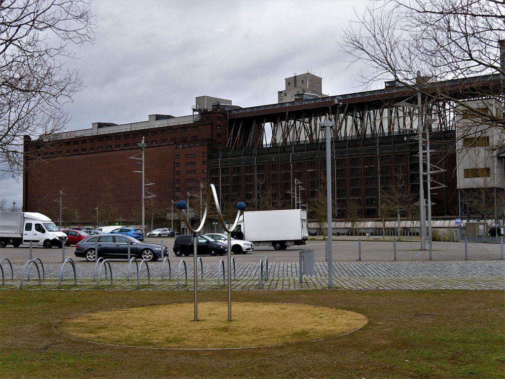 Getreideverkehrsanlage, Ein Parkplatz und Fahrradständer. Im Hintergrund ein Industriegebäude aus rotem Backstein.
